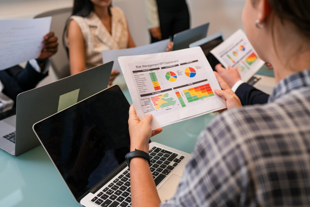 Employé d'entreprise tenant une feuille avec des statistiques de performances devant son ordinateur portable